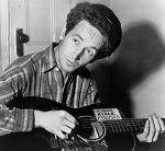 Black and white photo of Woody Guthrie playing the guitar.